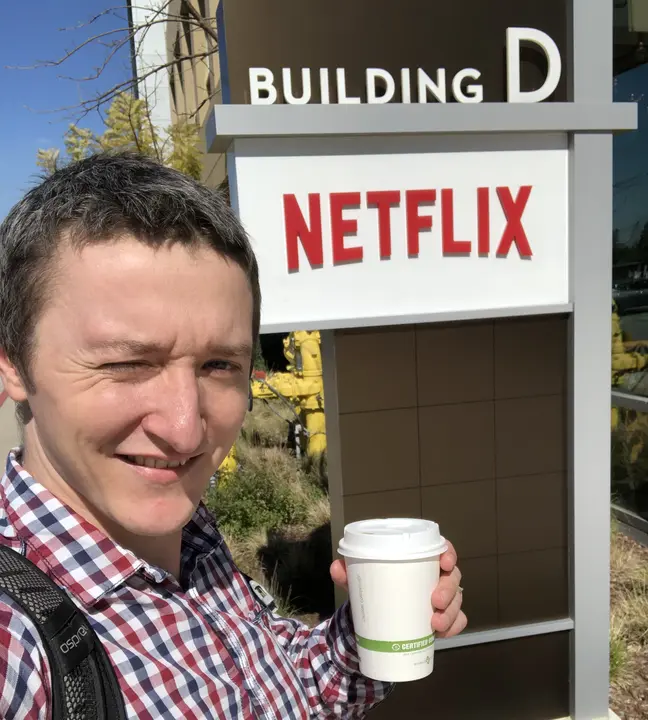 Vova with a cup of coffee at the Building D sign